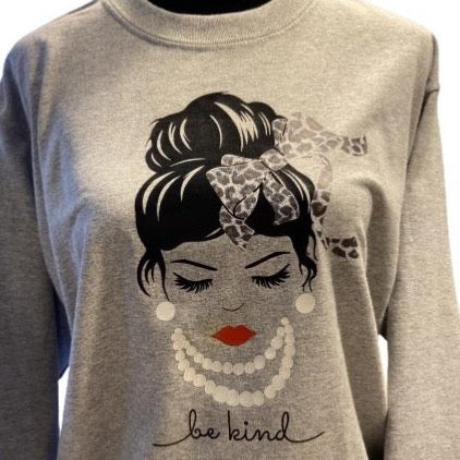 Woman with a bun and bow on a gray t-shirt, “Be Kind”.